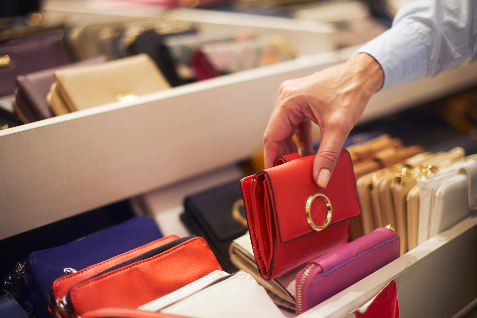 Senior woman picking up a red wallet from a rack in a bags and wallets store