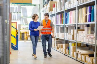 Manager discussing with foreman while walking by storage racks in large warehouse