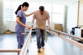 Patient takes his first steps using the orthopaedic parallel bars under the guidance of the physical therapist