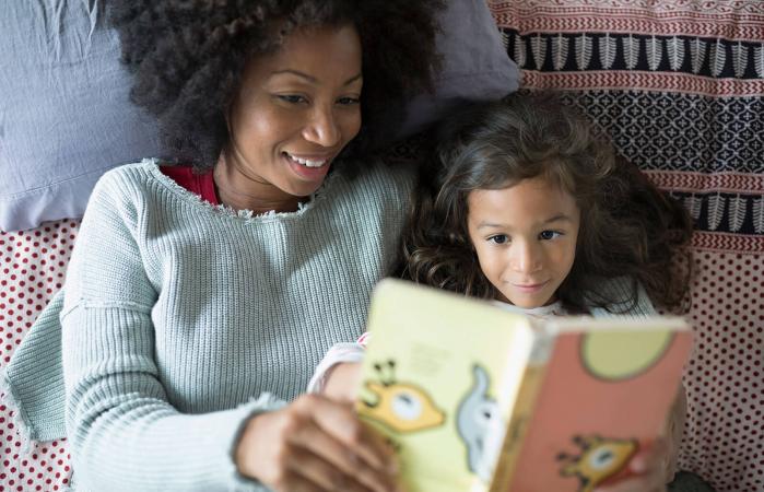 Madre e hija leyendo un libro en la cama