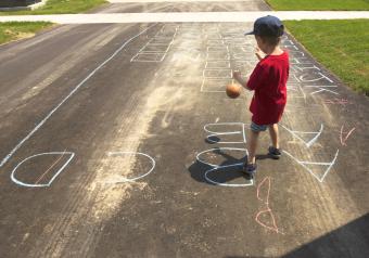 Boy playing with ball while standing on road with chalk drawing