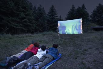 Young friends watching projection screen at campsite during night