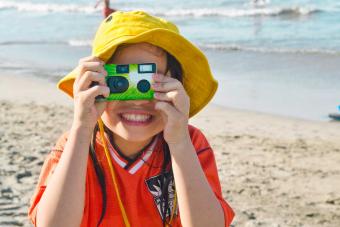 girl taking picture with disposable camera at beach