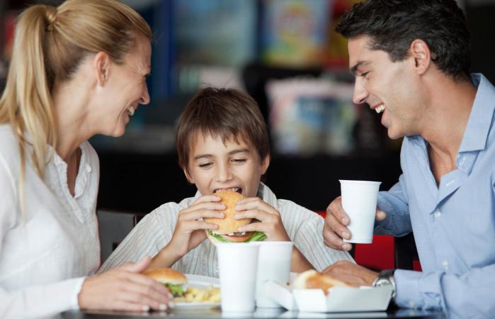 Boy eating hamburger with parents
