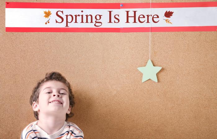Kindergarten boy sits against a cork board