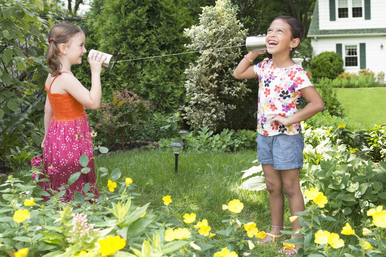 Girls using tin can telephone in backyard