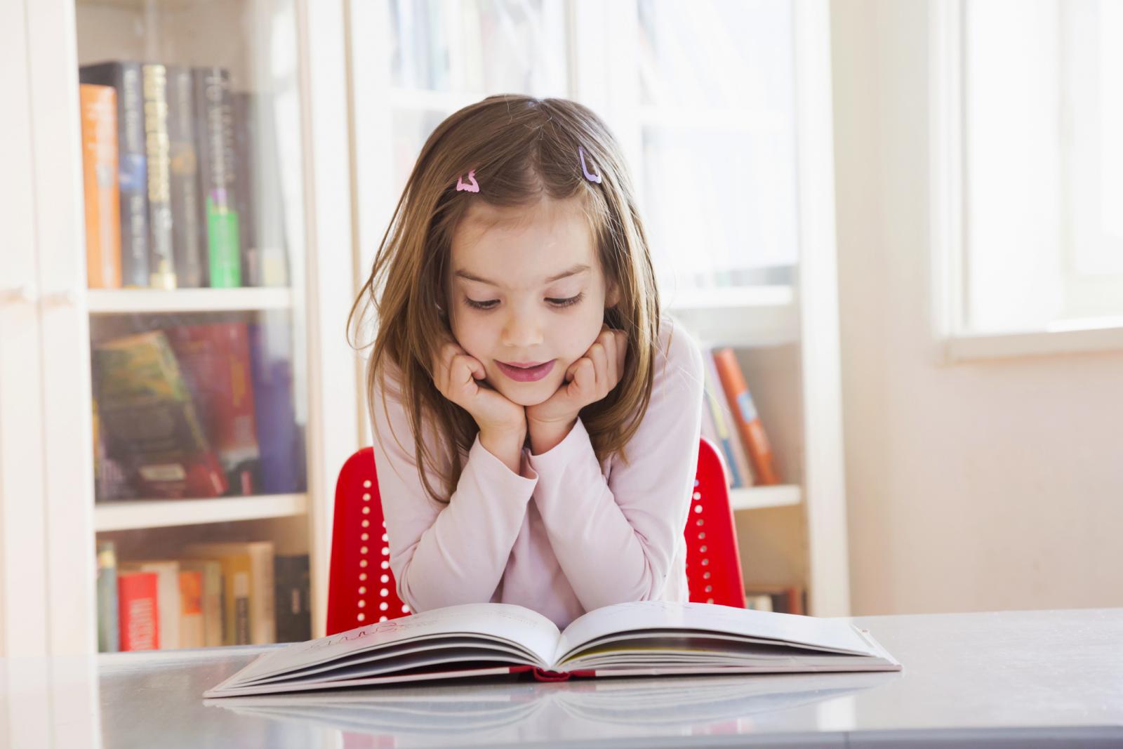 Portrait of little girl at table reading a book