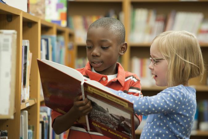 Boy and girl classmates sharing history book in library