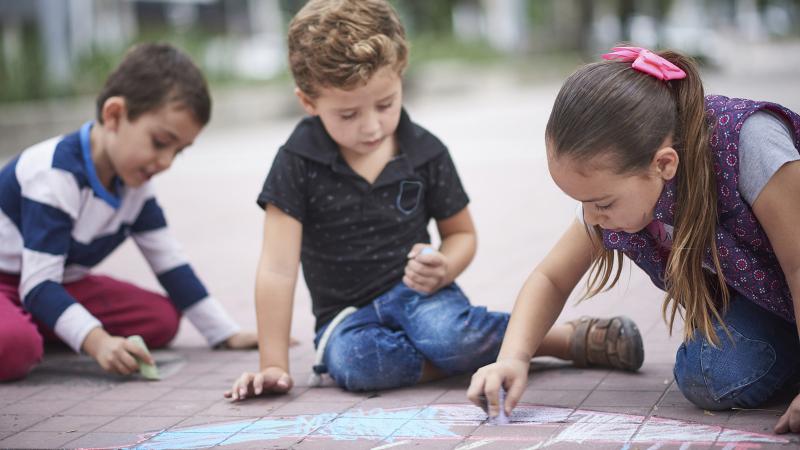 Hispanic boys and girl drawing with chalk on sidewalk