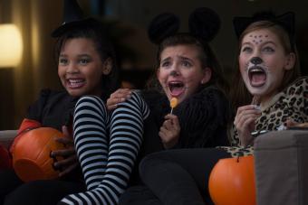 Girls in costumes watching scary movie together on Halloween