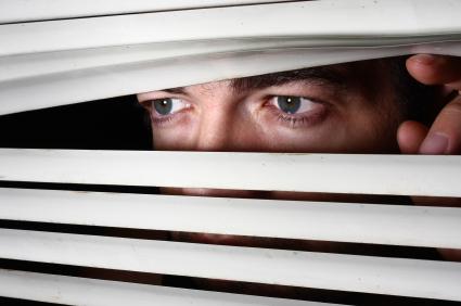 Frightened man peers through blinds
