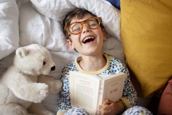 A 4 year old little boy having fun, laying on a bed 