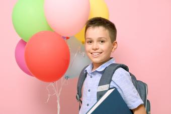 Schoolboy with backpack holding book and multicolored balloons