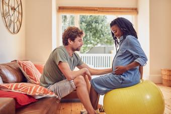 Pregnant woman sitting on exercise ball while husband supports her