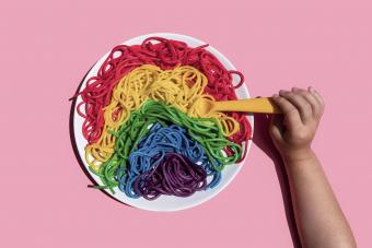 Hand of baby girl eating rainbow-colored spaghetti