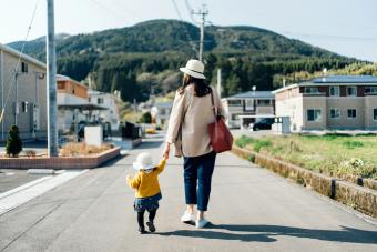 Mother and daughter with straw hat holding hands walking along town