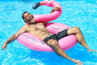 man floating in pool with pink flamingo float