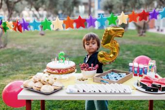 Little boy with golden balloon behind laid birthday table 