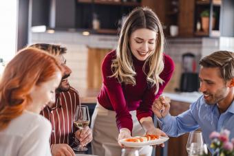 Friendly woman serving food to her friends at dining room