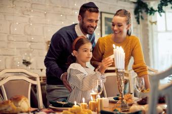 Happy Jewish family lightning the menorah before a meal at dining table