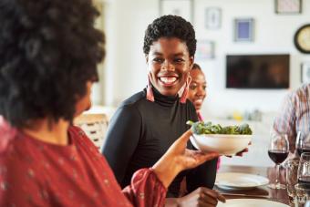 Woman passing food to smiling friend at party