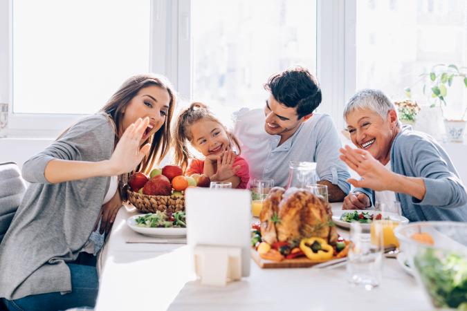 Family sitting at the dining table on Thanksgiving and communicating through a digital tablet
