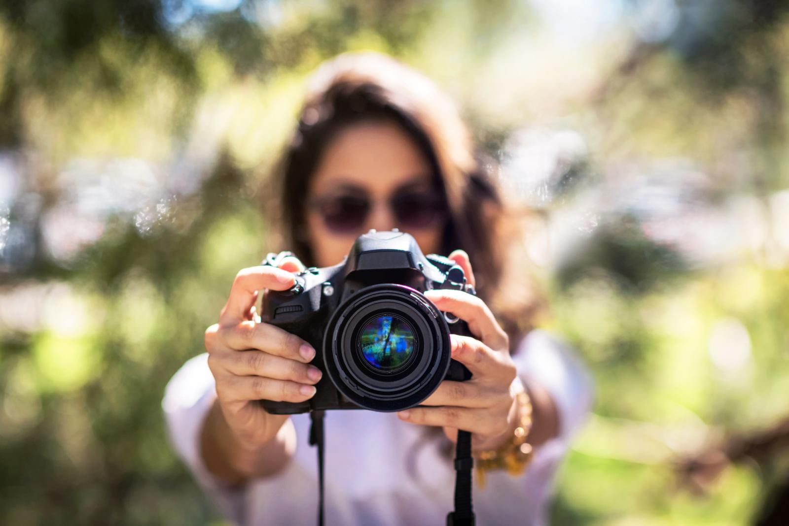 Woman wearing sunglasses holds a DSLR camera in front of her