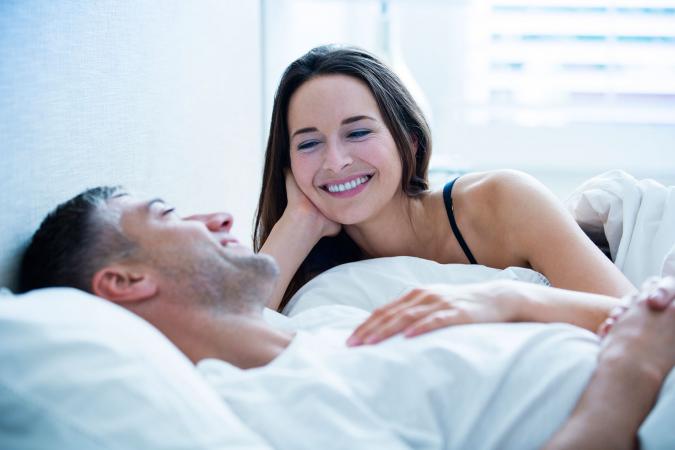 Smiling couple laying in bed talking