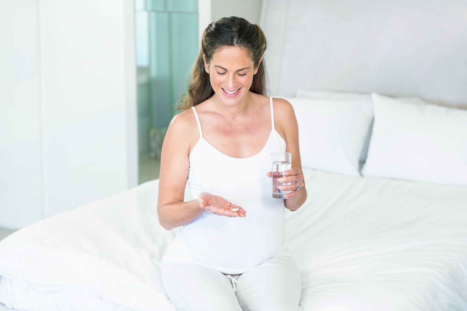 Pregnant woman taking antibiotics while sitting on bed