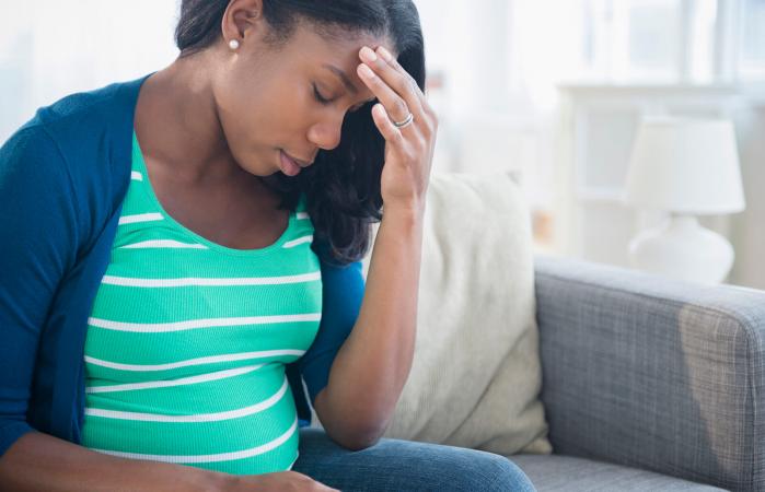 pregnant woman rubbing forehead on sofa