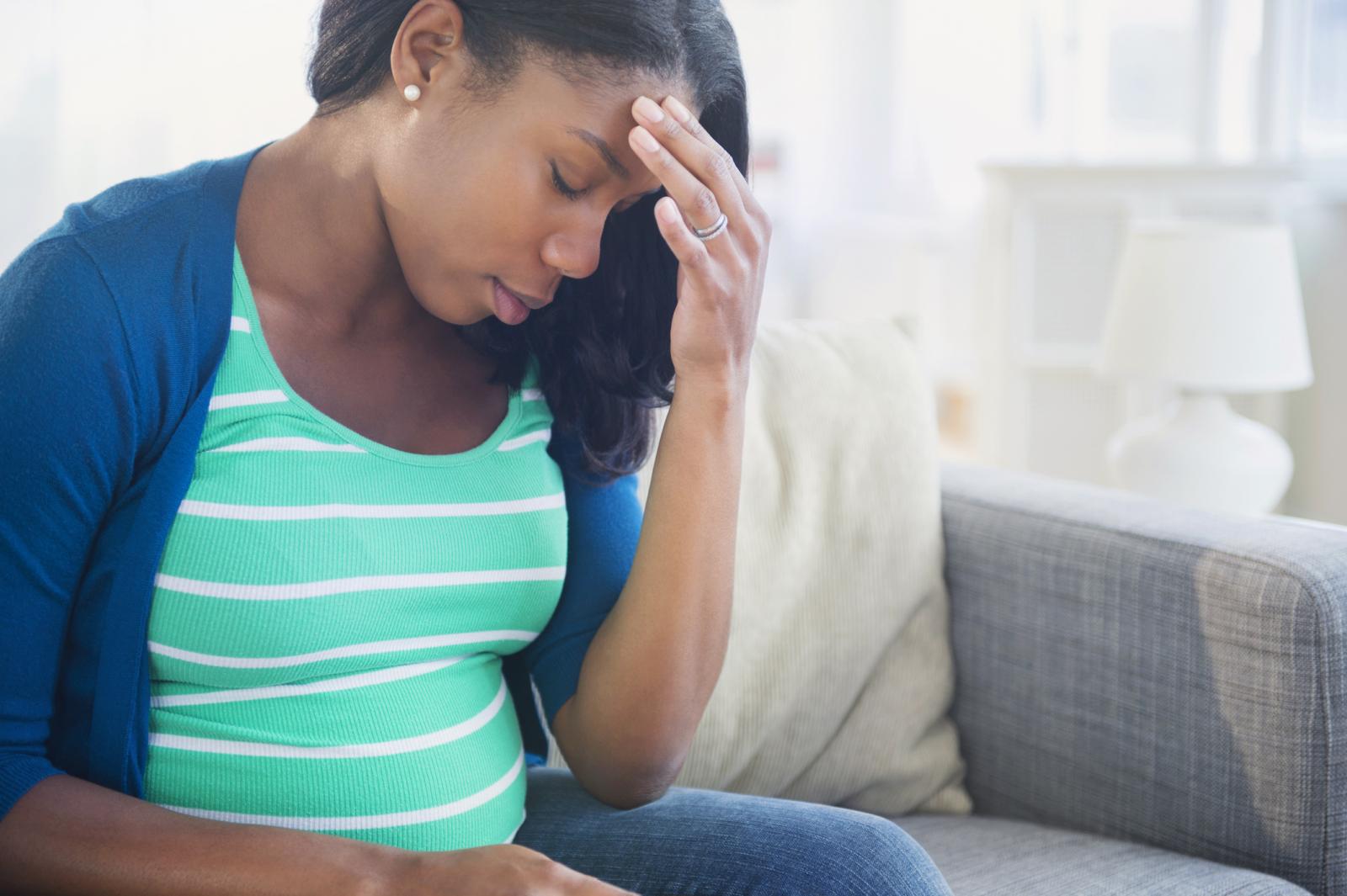 Anxious pregnant woman rubbing forehead on sofa