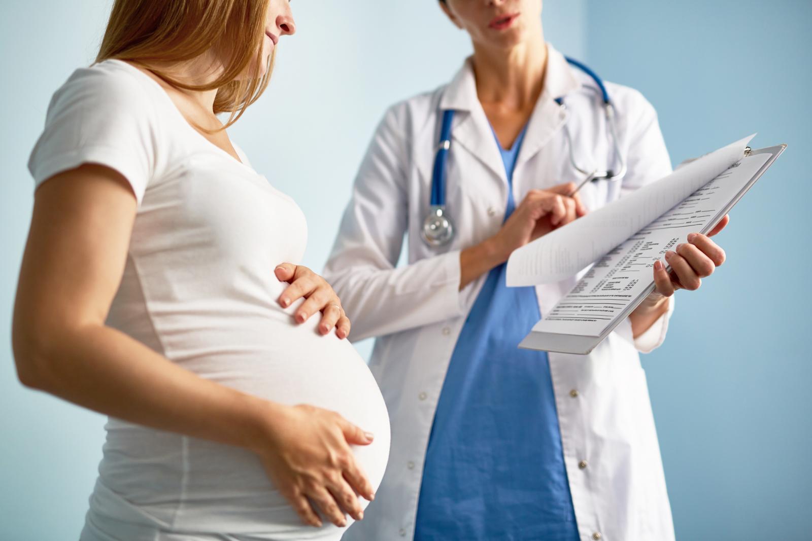 Pregnant female looking at paper with medical prescriptions held by her obstetrician