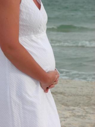 Pregnant woman in a white sundress at the beach