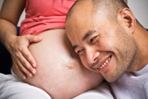 Happy man listening to his pregnant wife's belly