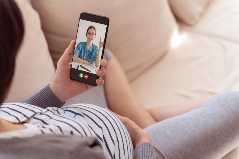 Woman sitting on sofa having online video chat with obstetrician doctor