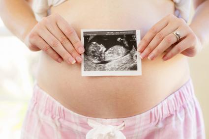 Woman holding sonogram over pregnant belly