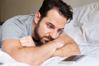 Hombre en la cama mirando al movil, esperando una llamada