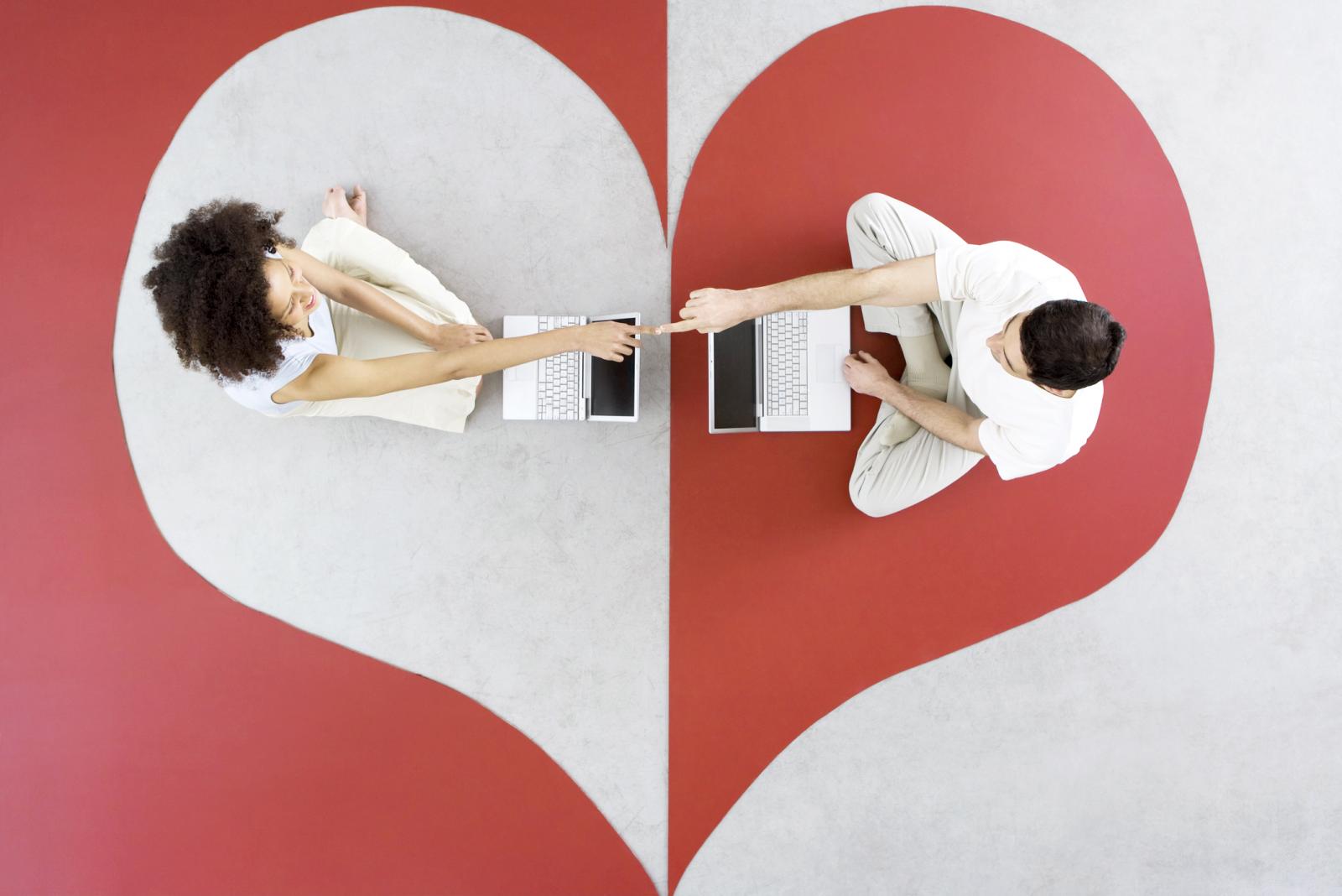 Pareja sentada con en el suelo dentro de un corazón con sus ordenadores