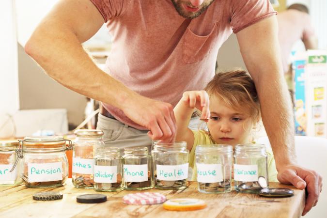 Father teaching daughter about finances by putting coins in jars