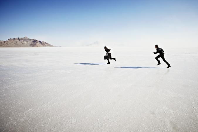 Businessman with briefcase on salt flats being chased by second businessman