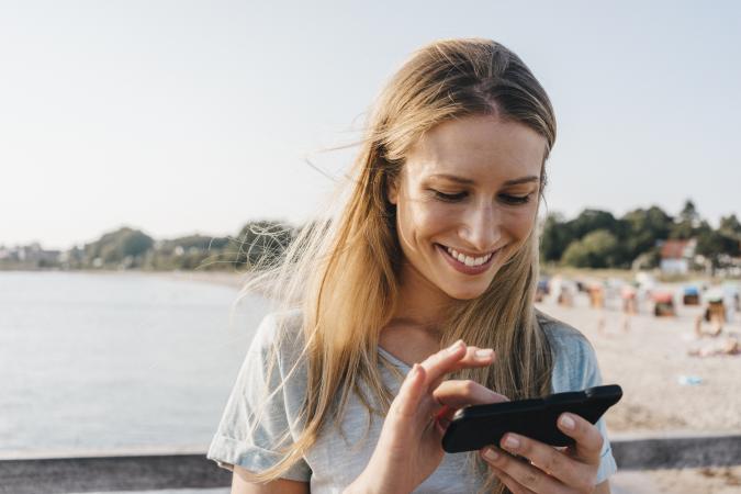 Happy woman using smartphone near beach