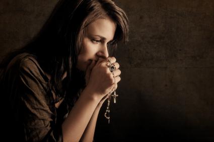 A woman praying holding a rosary