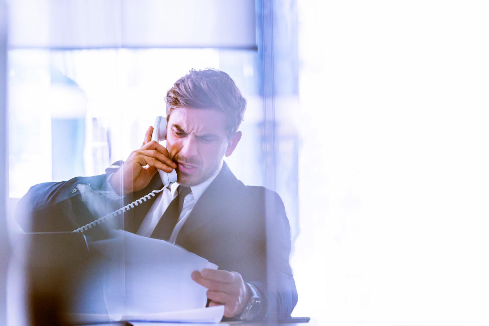 An anxious business executive talking to the phone while looking some paperwork