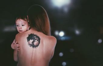 Mujer con tattoo en la espalda y con un bebé en sus brazos