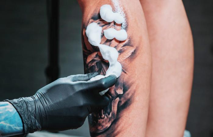 Tatuador aplicando crema en la pierna del cliente