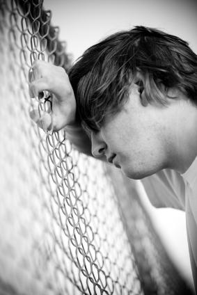 Image of a depressed teenager leaning on a fence 