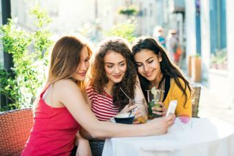 Teenager friends with smartphone sitting at the table in the outdoor cafe