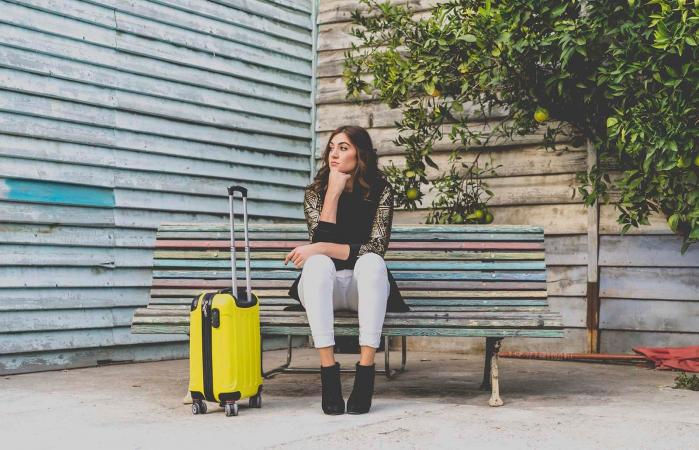 woman with yellow trolley bag waiting on a bench