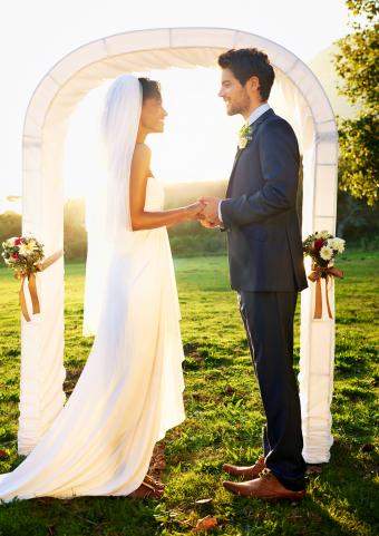 Bride and groom standing outside in front of the wedding arch