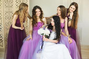 Bride holding a wedding bouquet and smiling while talking to her bridesmaids in purple dresses 